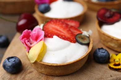 Photo of Sweet tartlets with berries and flowers on table, closeup. Delicious dessert