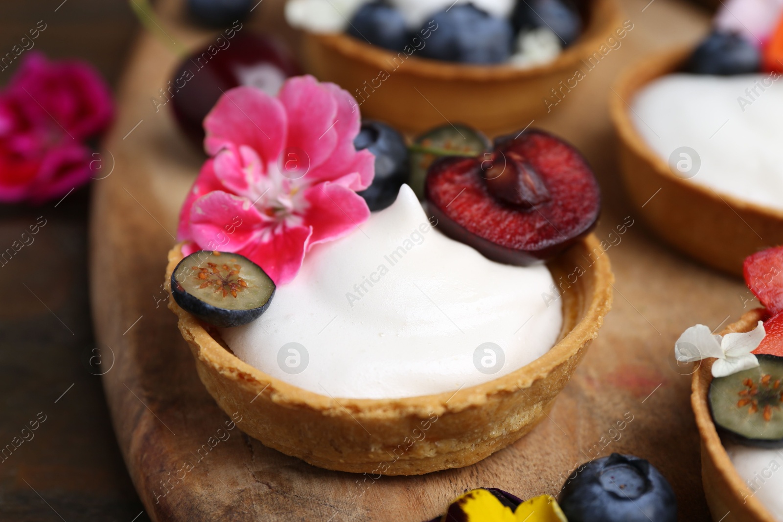Sweet tartlets with berries and flowers on table, closeup. Delicious dessert Photo of Sweet tartlets with berries and flowers on table, closeup. Delicious dessert