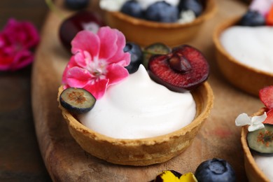 Photo of Sweet tartlets with berries and flowers on table, closeup. Delicious dessert