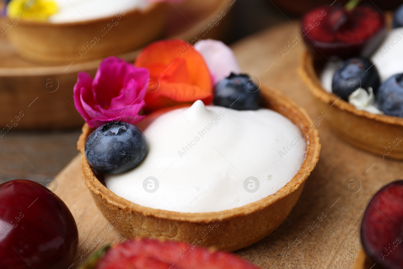 Sweet tartlets with berries and flowers on table, closeup. Delicious dessert Photo of Sweet tartlets with berries and flowers on table, closeup. Delicious dessert