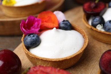 Photo of Sweet tartlets with berries and flowers on table, closeup. Delicious dessert