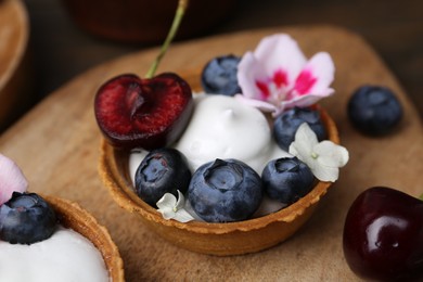 Photo of Sweet tartlets with berries and flowers on table, closeup. Delicious dessert