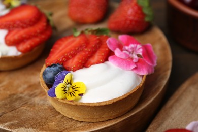 Photo of Sweet tartlets with berries and flowers on table, closeup. Delicious dessert