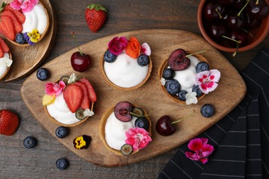 Photo of Sweet tartlets with berries and flowers on wooden table, flat lay. Delicious dessert