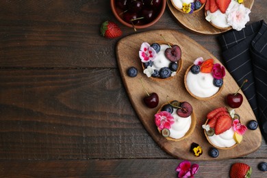 Photo of Sweet tartlets with berries and flowers on wooden table, flat lay with space for text. Delicious dessert