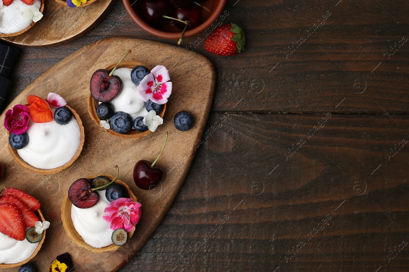 Sweet tartlets with berries and flowers on wooden table, flat lay with space for text. Delicious dessert Photo of Sweet tartlets with berries and flowers on wooden table, flat lay with space for text. Delicious dessert