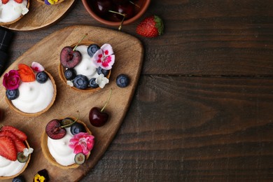 Photo of Sweet tartlets with berries and flowers on wooden table, flat lay with space for text. Delicious dessert