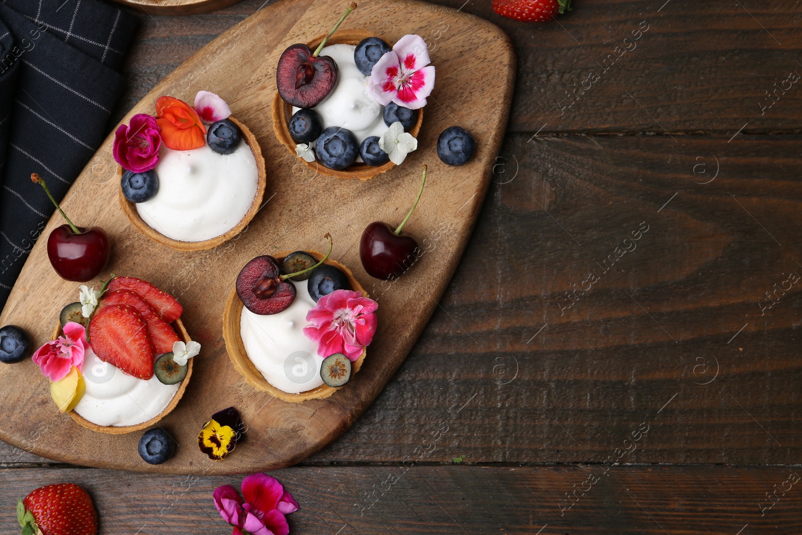 Sweet tartlets with berries and flowers on wooden table, flat lay with space for text. Delicious dessert Photo of Sweet tartlets with berries and flowers on wooden table, flat lay with space for text. Delicious dessert