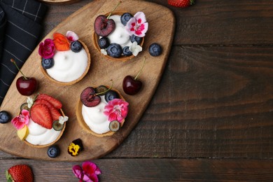 Photo of Sweet tartlets with berries and flowers on wooden table, flat lay with space for text. Delicious dessert