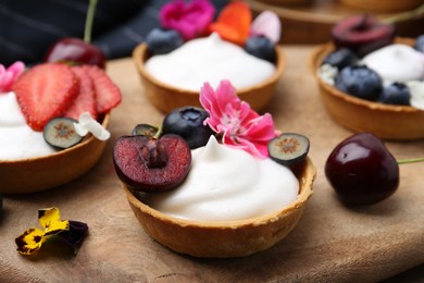 Photo of Sweet tartlets with berries and flowers on table, closeup. Delicious dessert