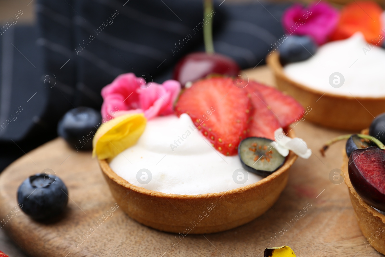 Sweet tartlets with berries and flowers on table, closeup. Delicious dessert Photo of Sweet tartlets with berries and flowers on table, closeup. Delicious dessert