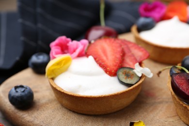 Photo of Sweet tartlets with berries and flowers on table, closeup. Delicious dessert