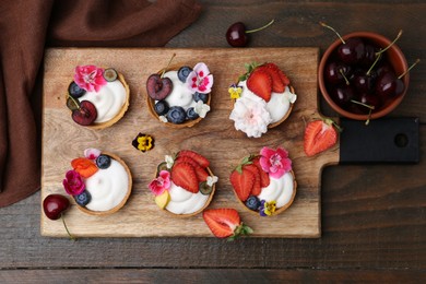 Photo of Sweet tartlets with berries and flowers on wooden table, flat lay. Delicious dessert
