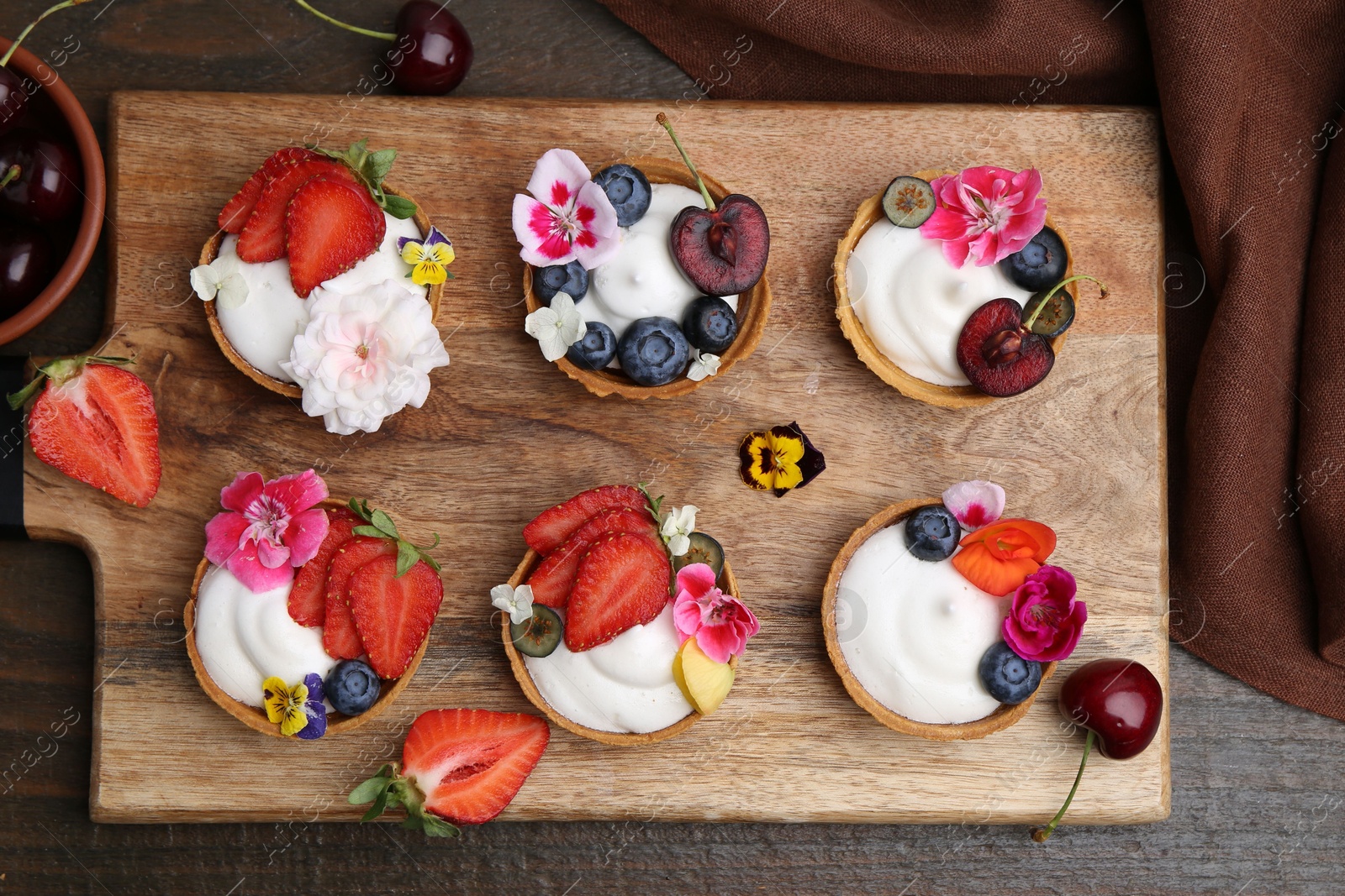 Sweet tartlets with berries and flowers on wooden table, flat lay. Delicious dessert Photo of Sweet tartlets with berries and flowers on wooden table, flat lay. Delicious dessert