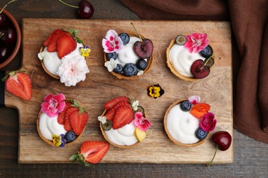 Photo of Sweet tartlets with berries and flowers on wooden table, flat lay. Delicious dessert