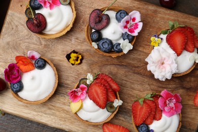 Photo of Sweet tartlets with berries and flowers on wooden table, top view. Delicious dessert
