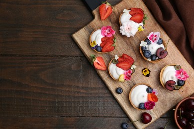 Photo of Sweet tartlets with berries and flowers on wooden table, flat lay with space for text. Delicious dessert