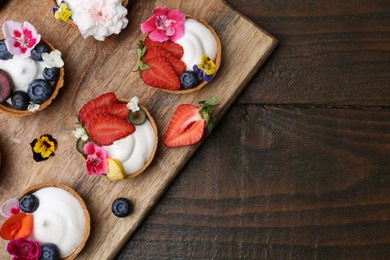 Photo of Sweet tartlets with berries and flowers on wooden table, top view with space for text. Delicious dessert