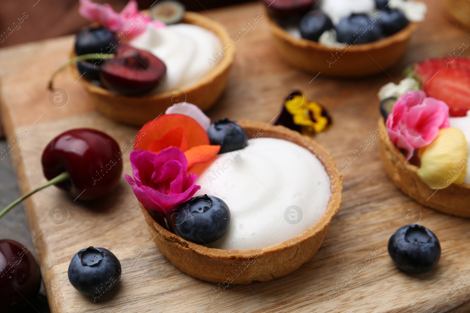 Sweet tartlets with berries and flowers on wooden board, closeup. Delicious dessert Photo of Sweet tartlets with berries and flowers on wooden board, closeup. Delicious dessert