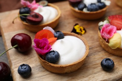 Photo of Sweet tartlets with berries and flowers on wooden board, closeup. Delicious dessert