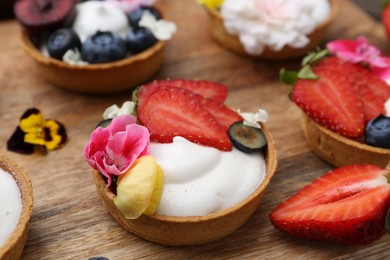 Photo of Sweet tartlets with berries and flowers on wooden board, closeup. Delicious dessert