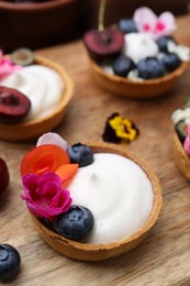 Photo of Sweet tartlets with berries and flowers on wooden board, closeup. Delicious dessert