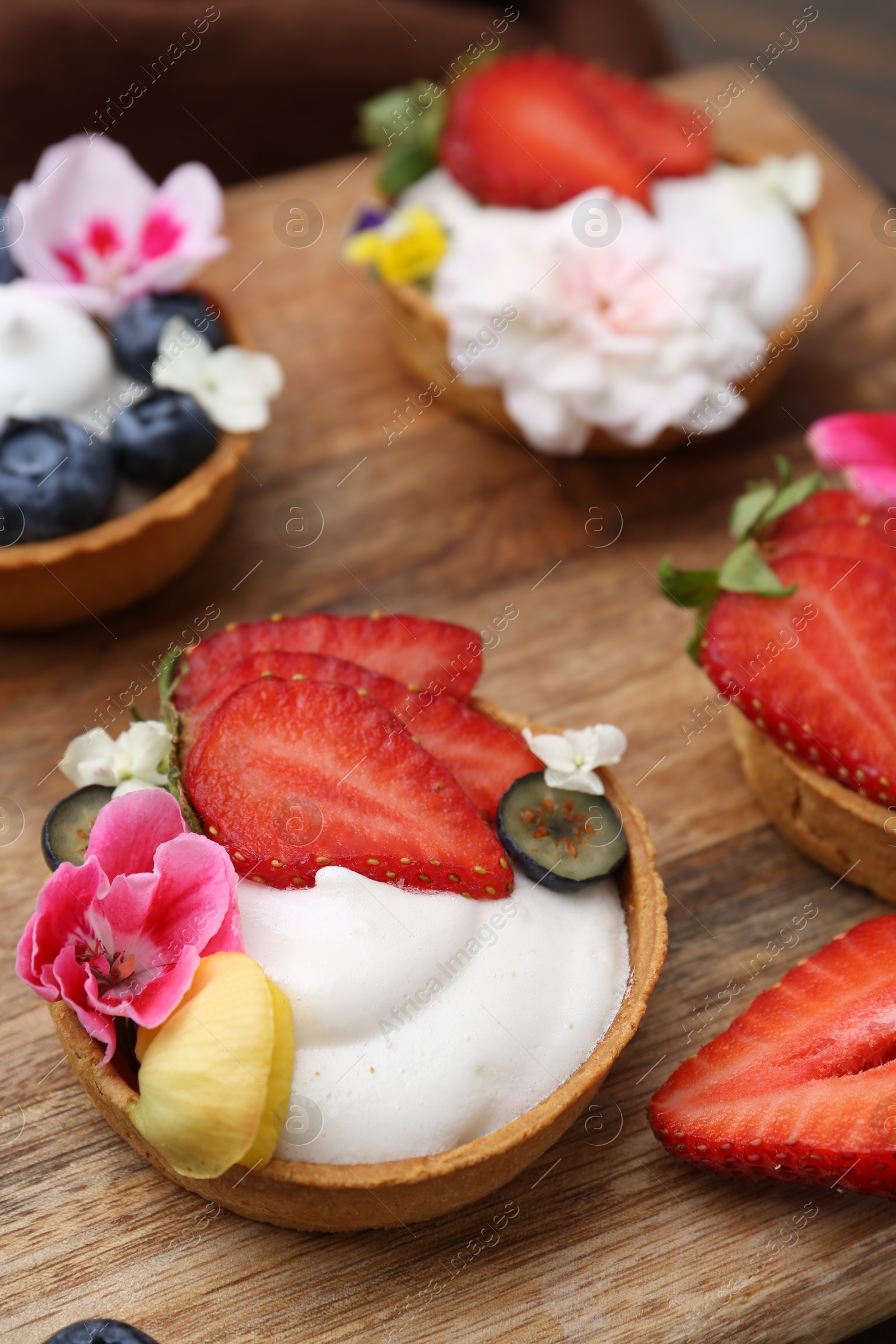 Sweet tartlets with berries and flowers on wooden board, closeup. Delicious dessert Photo of Sweet tartlets with berries and flowers on wooden board, closeup. Delicious dessert