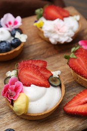 Photo of Sweet tartlets with berries and flowers on wooden board, closeup. Delicious dessert