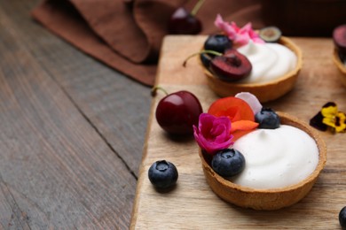 Photo of Sweet tartlets with berries and flowers on wooden table, closeup. Delicious dessert