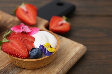 Photo of Sweet tartlet with berries and flowers on wooden table, closeup. Delicious dessert
