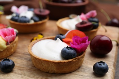 Photo of Sweet tartlets with berries and flowers on wooden board, closeup. Delicious dessert