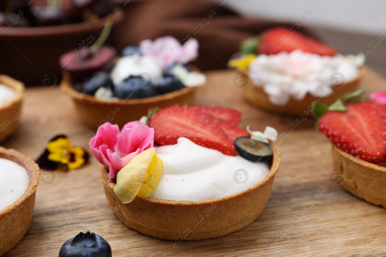 Sweet tartlets with berries and flowers on wooden board, closeup. Delicious dessert Photo of Sweet tartlets with berries and flowers on wooden board, closeup. Delicious dessert