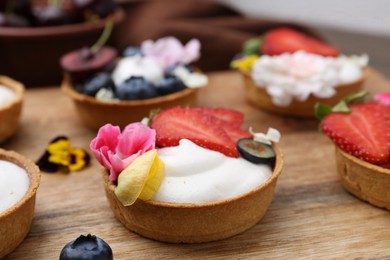 Photo of Sweet tartlets with berries and flowers on wooden board, closeup. Delicious dessert
