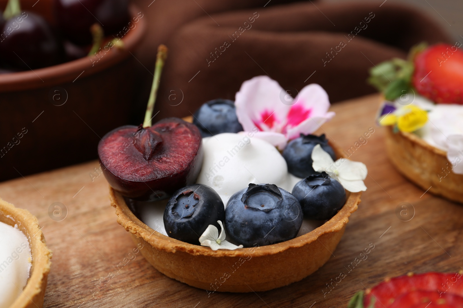 Sweet tartlet with berries and flowers on wooden board, closeup. Delicious dessert Photo of Sweet tartlet with berries and flowers on wooden board, closeup. Delicious dessert