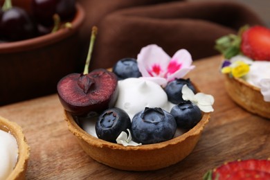 Photo of Sweet tartlet with berries and flowers on wooden board, closeup. Delicious dessert