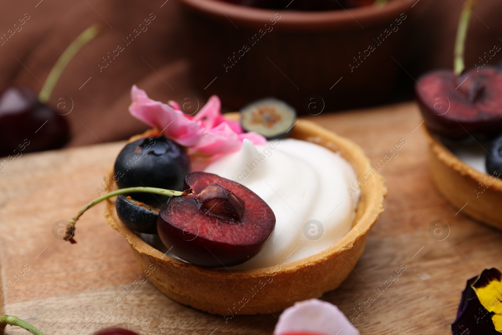 Sweet tartlet with berries and flower on wooden board, closeup. Delicious dessert Photo of Sweet tartlet with berries and flower on wooden board, closeup. Delicious dessert