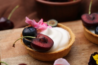 Photo of Sweet tartlet with berries and flower on wooden board, closeup. Delicious dessert