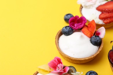 Photo of Sweet tartlets with berries and flowers on yellow background, closeup with space for text. Delicious dessert