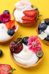 Photo of Sweet tartlets with berries and flowers on yellow background, above view. Delicious dessert