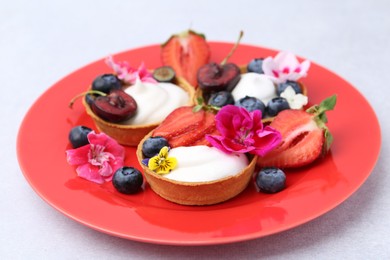 Photo of Sweet tartlets with berries and flowers on grey table, closeup. Delicious dessert