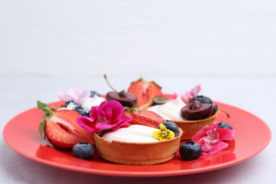 Photo of Sweet tartlets with berries and flowers on grey table against light background, closeup. Delicious dessert