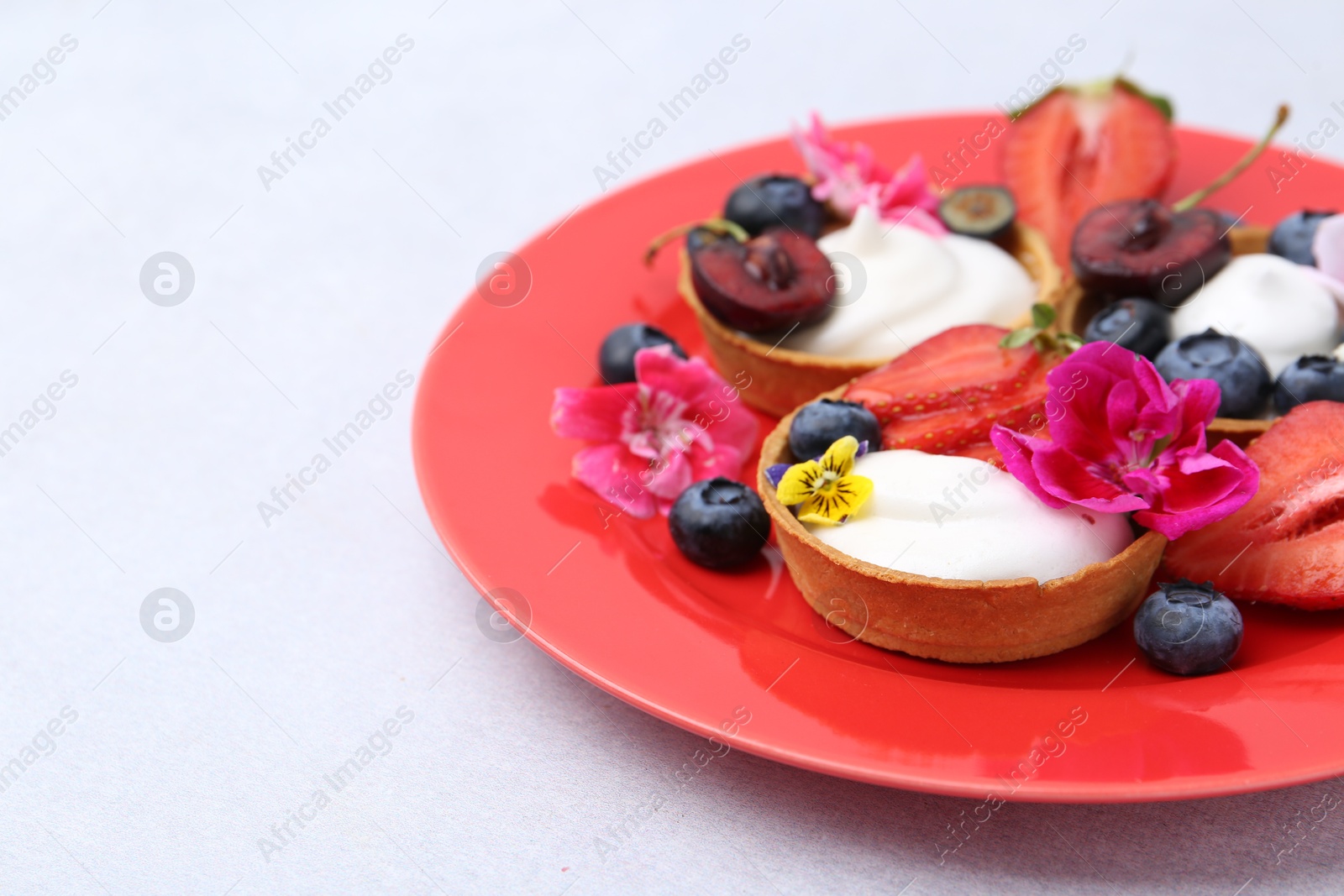 Sweet tartlets with berries and flowers on grey table, closeup. Delicious dessert Photo of Sweet tartlets with berries and flowers on grey table, closeup. Delicious dessert