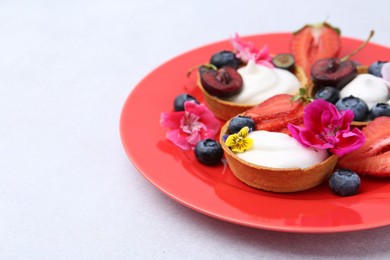 Photo of Sweet tartlets with berries and flowers on grey table, closeup. Delicious dessert