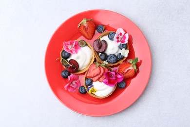 Photo of Sweet tartlets with berries and flowers on grey table, top view. Delicious dessert