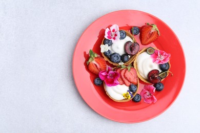 Photo of Sweet tartlets with berries and flowers on grey table, top view with space for text. Delicious dessert