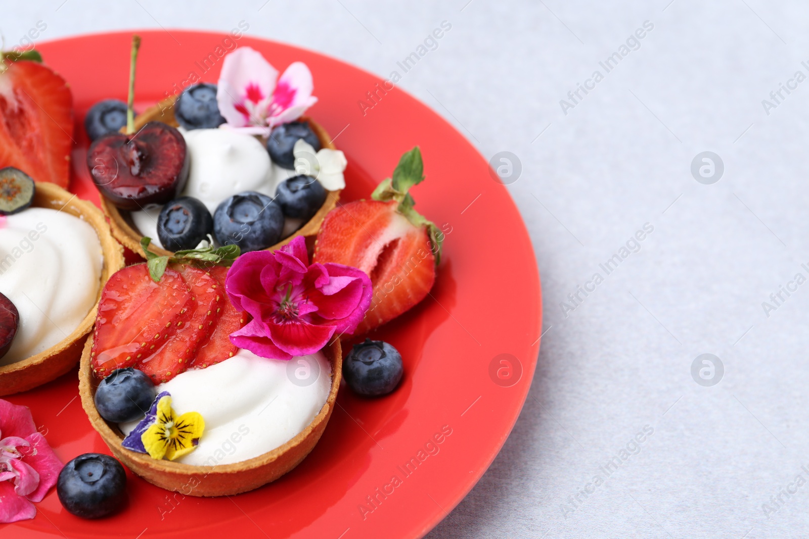 Sweet tartlets with berries and flowers on grey table, closeup. Delicious dessert Photo of Sweet tartlets with berries and flowers on grey table, closeup. Delicious dessert