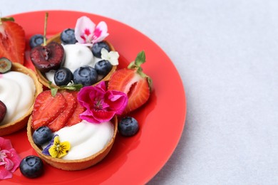 Photo of Sweet tartlets with berries and flowers on grey table, closeup. Delicious dessert