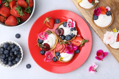 Photo of Sweet tartlets with berries and flowers on grey table, flat lay. Delicious dessert
