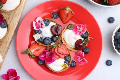 Photo of Sweet tartlets with berries and flowers on grey table, flat lay. Delicious dessert