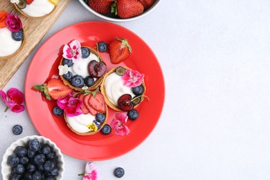 Photo of Sweet tartlets with berries and flowers on light grey table, flat lay with space for text. Delicious dessert